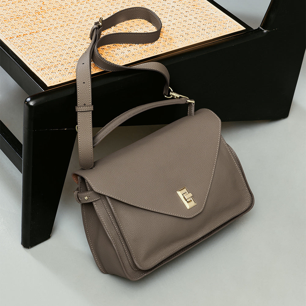 Brown leather handbag with gold clasp on a light gray surface